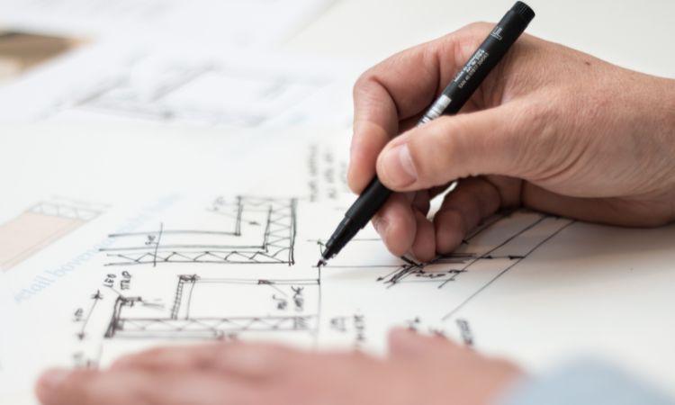 Main dessinant un plan d\'aménagement de bureaux au stylo