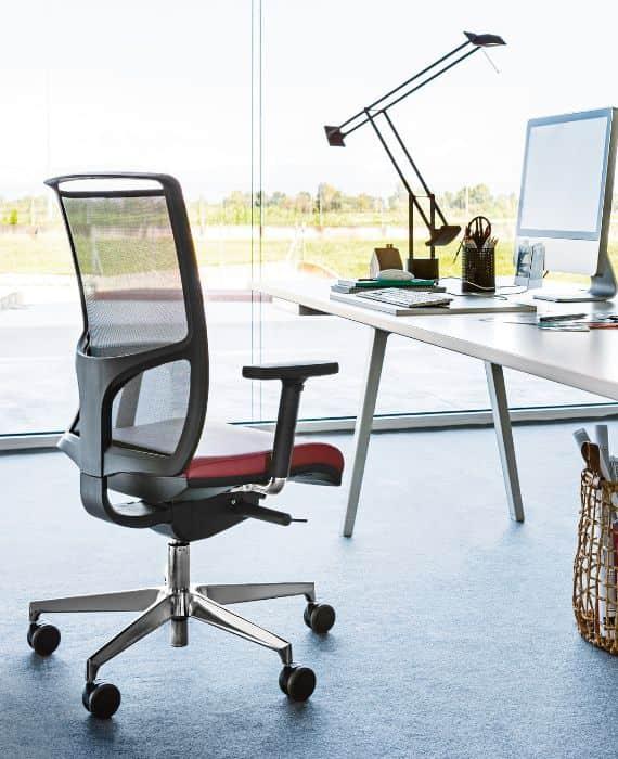 Poste de travail avec fauteuil ergonomique à assise rouge devant des baies vitrées